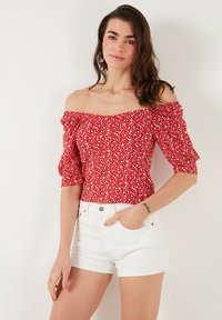 Red off-the-shoulder top with puff sleeves, featuring a floral pattern; paired with white denim shorts. Smooth fabric, fitted design.