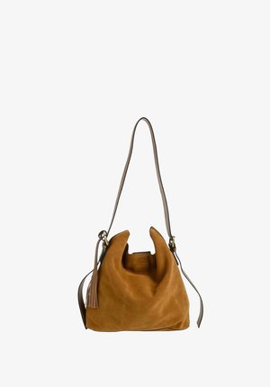 Sac épaule en daim marron avec bandoulière longue réglable et détail pompon sur le côté, forme souple et décontractée, sur fond blanc.