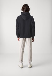 Felpa nera con cappuccio, dalla vestibilità rilassata, texture morbida e maniche lunghe, abbinata a pantaloni grigi chiari arrotolati e sneakers bianche.