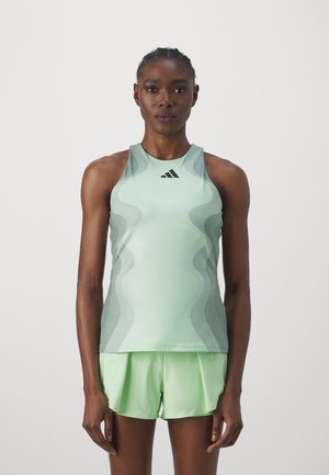 Débardeur de sport vert clair avec un motif de texture ondulée, logo sur la poitrine, associé à un short coordonné dans une teinte similaire.