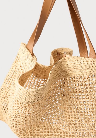 Πλεκτή μπεζ τσάντα ώμου με ανοιχτό σχέδιο ύφανσης και φαρδιές λουριά από ταμπά δέρμα σε ουδέτερο φόντο.