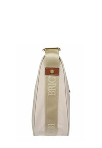 Borsa beige vista laterale verticale con ampia tracolla dorata, recante la scritta bianca "BRIC’S" e una piccola toppa in pelle marrone con un bottone dorato.