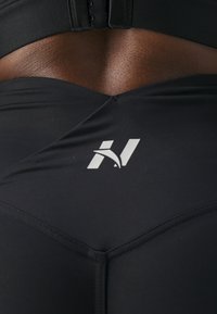 Leggings sportivi neri con un design aderente e texture liscia. Un logo bianco è visibile vicino alla vita, sottolineando l'identità del marchio.