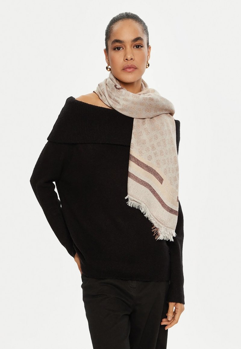 Suéter negro de punto oversized con diseño de hombros al aire, combinado con una bufanda beige claro con un patrón sutil y bordes con flecos.
