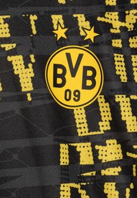 Must kärgiga jägijärgsest mustrist, millel on kollane abstraktne muster, sisaldab ringikujulist logo, millel on "BVB 09" ja kaks tähte selle kohal. Tekstuuritud kangas kaasaegse disainiga.