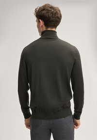 Dunkelgrüner Rollkragenpullover aus glattem Strickmaterial, mit langen Ärmeln und schmalem Saum, kombiniert mit strukturierten grauen Hosen.