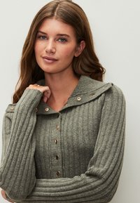 Olivgrüner, gerippter Cardigan mit Knopfleiste und Kragen. Verfügt über goldfarbene Knöpfe und strukturierten Stoff mit langen Ärmeln.