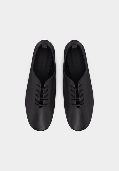 Paire de chaussures à lacets en cuir noir avec bouts ronds et languettes, vues de dessus sur un fond clair uni.