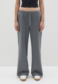 Graue, weit geschnittene Jogginghosen aus weichem, strukturiertem Stoff, mit einem elastischen Bund und Kordelzug, kombiniert mit weißen Turnschuhen.