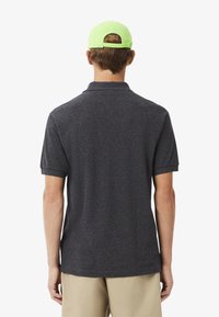 Kolsvart polo-shirt med klassisk krage och korta ärmar, matchad med en klargrön keps. Tyget ser slätt ut med en subtil textur.
