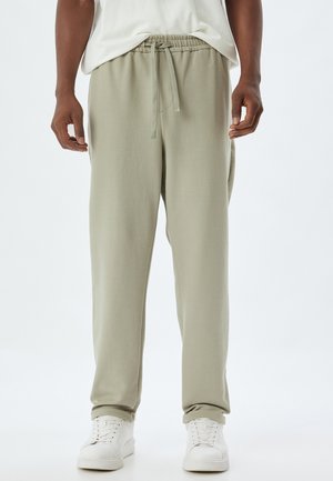 Lys grønne sweatpants med snøre i taljen, der har en glat tekstur og tapered fit, parret med hvide sneakers.