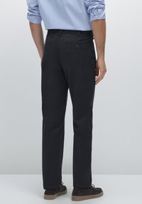 Black trousers made of a smooth fabric, featuring a straight cut, two back pockets with buttons, and subtle texture details.