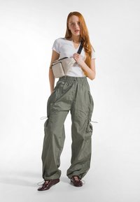 Cargo bukser i oliet grøn, lavet af letvægtsstof med snøre i taljen, kombineret med en hvid V-hals T-shirt og en beige crossbody-taske.