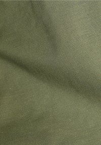Gros plan sur un tissu texturé vert olive avec des fils fins et serrés, et des ombres subtiles montrant des plis.