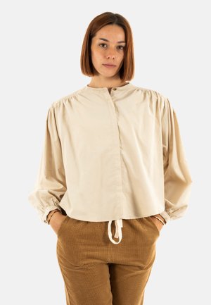Blouse beige à manches longues avec un col rond, des épaules froncées et des poignets élastiques. La blouse a une coupe décontractée et un ourlet avec cordon de serrage.