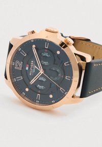 Στρογγυλό ρολόι χειρός Tommy Hilfiger σε χρυσό τόνο με μαύρο καντράν, τρία υποκαντράν και μαύρη δερμάτινη λωρίδα με καφέ ραφή.