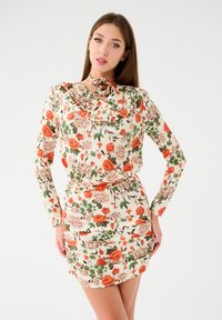 Kwiatowa sukienka z długimi rękawami, o kremowym tle, z pomarańczowymi i różowymi kwiatami oraz dekoltem w kształcie czołówki. Dopasowana z marszczeniem w talii.