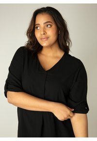 Zwarte blouse met een V-hals, opgerolde korte mouwen en een relaxte pasvorm. Soepele stof met subtiele drapering en knoopaccenten op de mouwen.