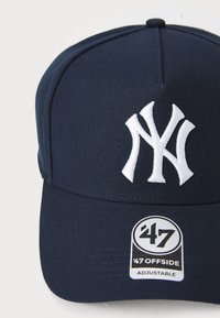 Navy blue baseball cap made of fabric with a white embroidered logo on the front. Features an adjustable strap and a branded tag.