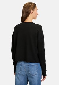 Svart croppad tröja med rund hals, ribbade muddars och nederkant, i kombination med blekta blå jeans med bakfickor och en lätt tvättning.