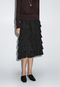 Black ruffled skirt with layered fabric, paired with a dark sweater and black slip-on shoes. The fabric has a smooth texture.