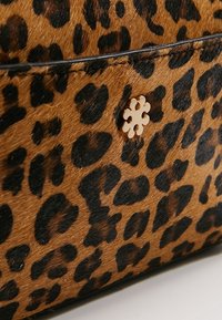 Håndtaske med leopardprint i brun og sort farveskema, med en glat, pelsagtig tekstur og et dekorativt emblem i guld.