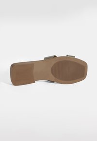 Semelle de sandale en caoutchouc marron avec un motif de grip texturé, dotée d'un design lisse et plat, ainsi que de deux larges sangles en vert olive.
