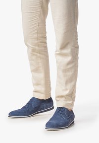 Marineblaue Wildlederschuhe mit glatter Oberfläche, klassischem Schnürdesign und weißer Gummisohle, kombiniert mit hellbeigen Hosen.