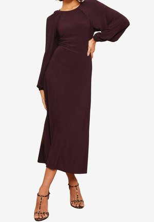 Dlouhé fialové šaty s přiléhavým živůtkem a splývavými rukávy, vyrobené z hladké látky. Kombinované s páskovými sandály se zvířecím potiskem.