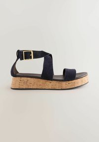 Sandale din velur bleumarin cu talpă din plută. Au o curea lată peste picior și o curea reglabilă la glezna cu o cataramă aurie.