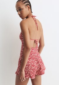 Costume da bagno con motivo floreale rosso, design con collo all'americana e schiena aperta. Presenta orlo arricciato e dettaglio di fiocco sul retro. Tessuto con texture liscia.