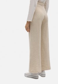 Pantalones beige de pierna ancha hechos de tejido suave, con cintura alta y bordes limpios. Combinados con zapatillas blancas.