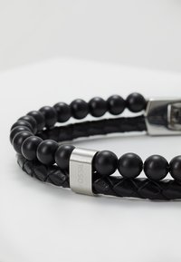 Black leather and bead bracelet featuring a braided design, smooth round beads, and a rectangular metallic clasp with the "Fossil" logo.