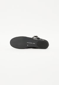 Black sandal with a flat sole, adjustable strap, and textured upper. Notable features include embossed branding and a smooth finish.