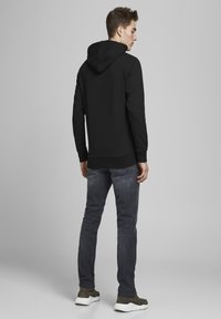 Hanorac negru cu glugă ajustabilă, manșete și tiv cu bordură; asortat cu blugi gri închis și adidași verzi. Design simplu, fără modele vizibile.