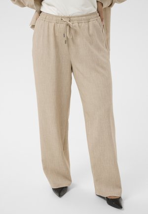 Pantalon beige à jambes larges avec taille élastique et cordon, porté avec des chaussures noires pointues et un haut blanc partiellement visible.
