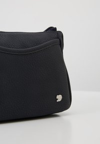 Borsa nera in pelle con superficie testurizzata, design curvo e un accento logo argentato sul lato. Presenta una chiusura a zip nella parte superiore.