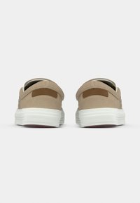 Paire de baskets en daim beige vue de dos avec semelles blanches et languette marron au talon sur un fond clair uni.