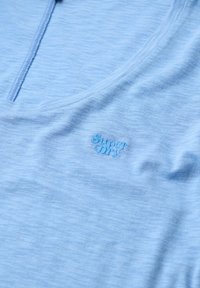 Jasnoniebieska koszula z miękkiego materiału, o subtelnej fakturze i małym haftowanym logo w dopasowanym odcieniu niebieskiego.