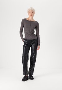 Haut gris à manches longues avec un col rond et une couture centrale, associé à un pantalon en cuir noir brillant et des chaussures noires.
