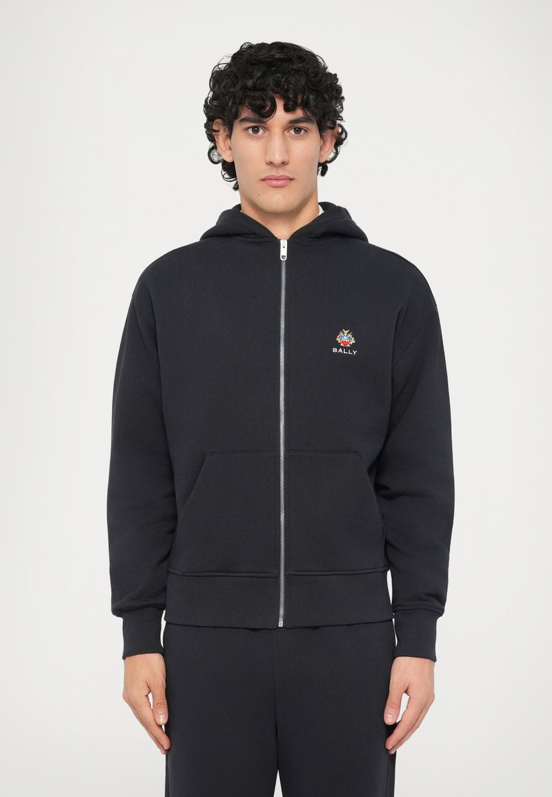 Sudadera con cremallera negra hecha de mezcla de algodón, con un bolsillo frontal y un logotipo bordado en el lado izquierdo del pecho. Puños y dobladillo acanalados.