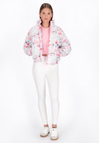 Padded, zapinana kurtka w białym kolorze z różowym i niebieskim wzorem tie-dye; posiada wysoki kołnierz i elastyczne mankiety; zestawiona z białymi legginsami.
