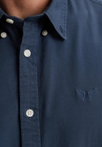 navyfarbendes Hemd mit Kn�öpfen aus Baumwolle, ausgestattet mit einem Kragen, gesticktem Flügel-Logo und kontrastierenden weißen Knöpfen. Glatte Textur.