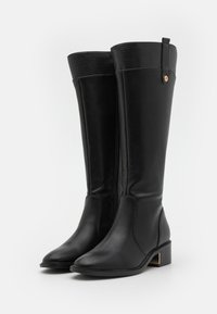 Bottes noires montantes en cuir lisse, avec une fermeture éclair, des accents texturés discrets en haut et un petit talon carré avec un détail doré.
