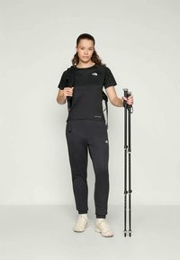 Crni sportski outfit sastavljen od kratkotrajne majice i uskih hlača, uparen s planinarskim štapovima i svijetlim tenisicama.