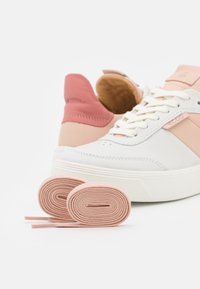Baskets blanches avec des accents roses, cuir texturé, lacets plats, bout arrondi et semelle épaisse blanche. Deux lacets roses sont présentés à l'avant.