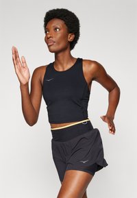 Svart atletisk crop top med racerback-design och silverlogotyp. Kombinerad med svarta löparshorts med elastisk midja och gul accent.