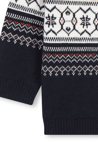 Pull marine avec des motifs géométriques blancs, rouges et noirs. Manches et ourlets côtelés, texture douce, présentant des motifs de flocons de neige et des zigzags.