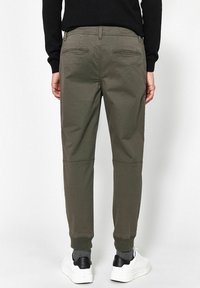 Olivově zelené zúžené kalhoty s elastickými manžetami, s zadními kapsami a hladkým povrchem, nošeny s bílými teniskami.