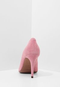 Chaussure à talon haut en daim rose avec un bout pointu et un talon aiguille élancé. Texture lisse et lignes épurées, présentant un branding minimal sur la semelle.